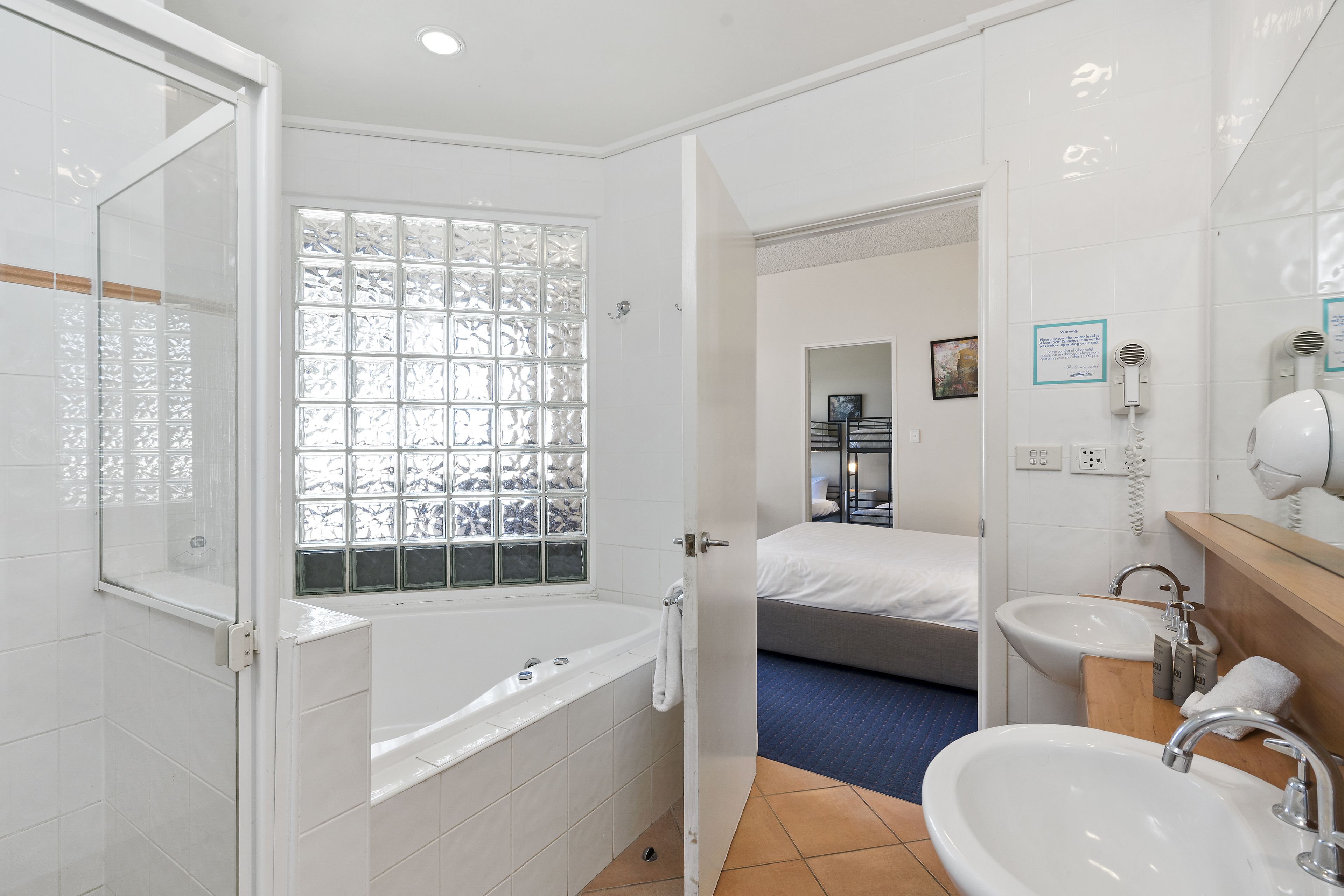 Ein Hotelbad mit Badewanne, Fenster mit dekorativem Gitter, einem Bett, einem Waschbecken und einem Spiegel.
