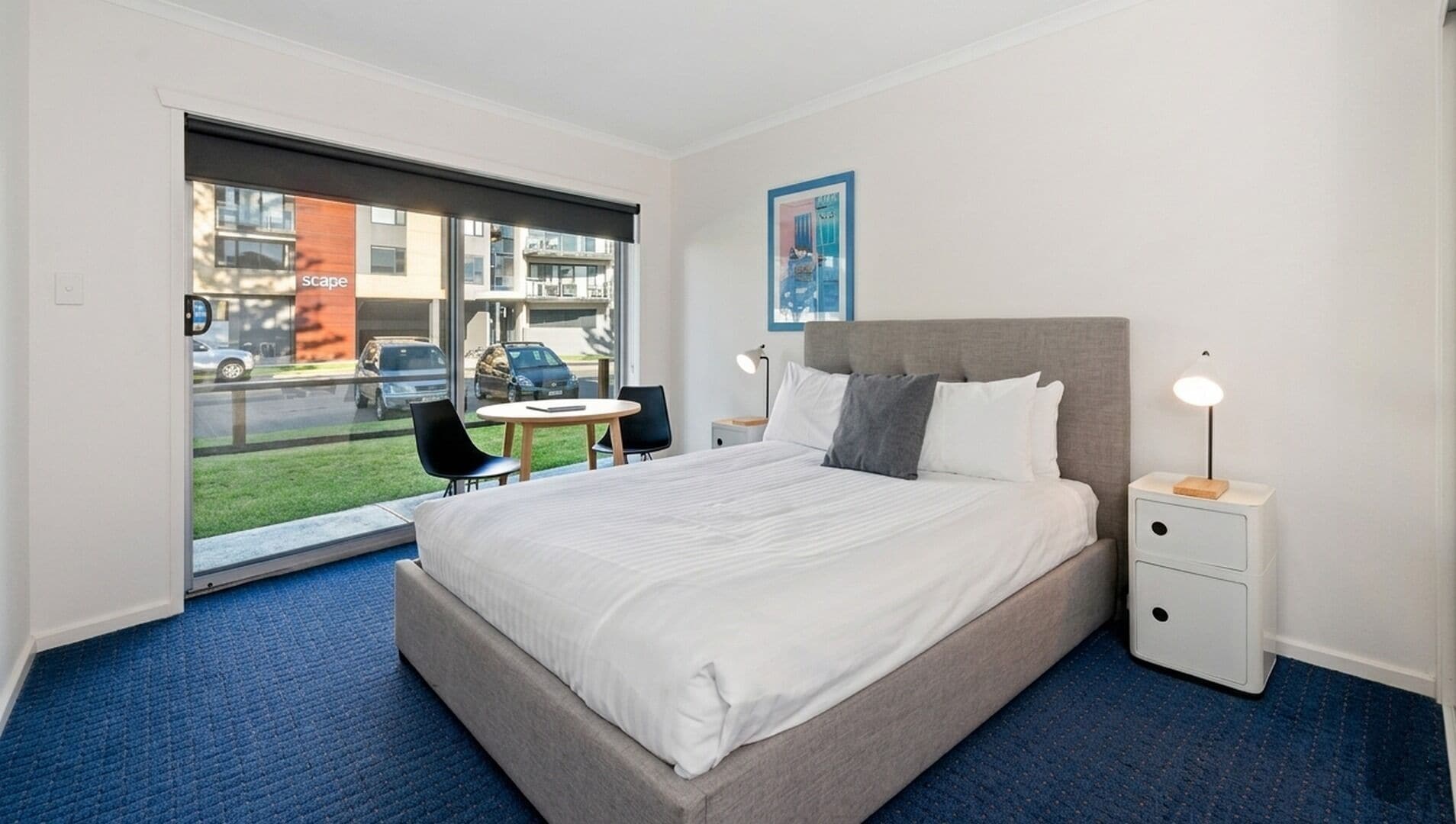 A hotel room with a bed, bedside tables, a desk, a chair, and a window with a view of the street.