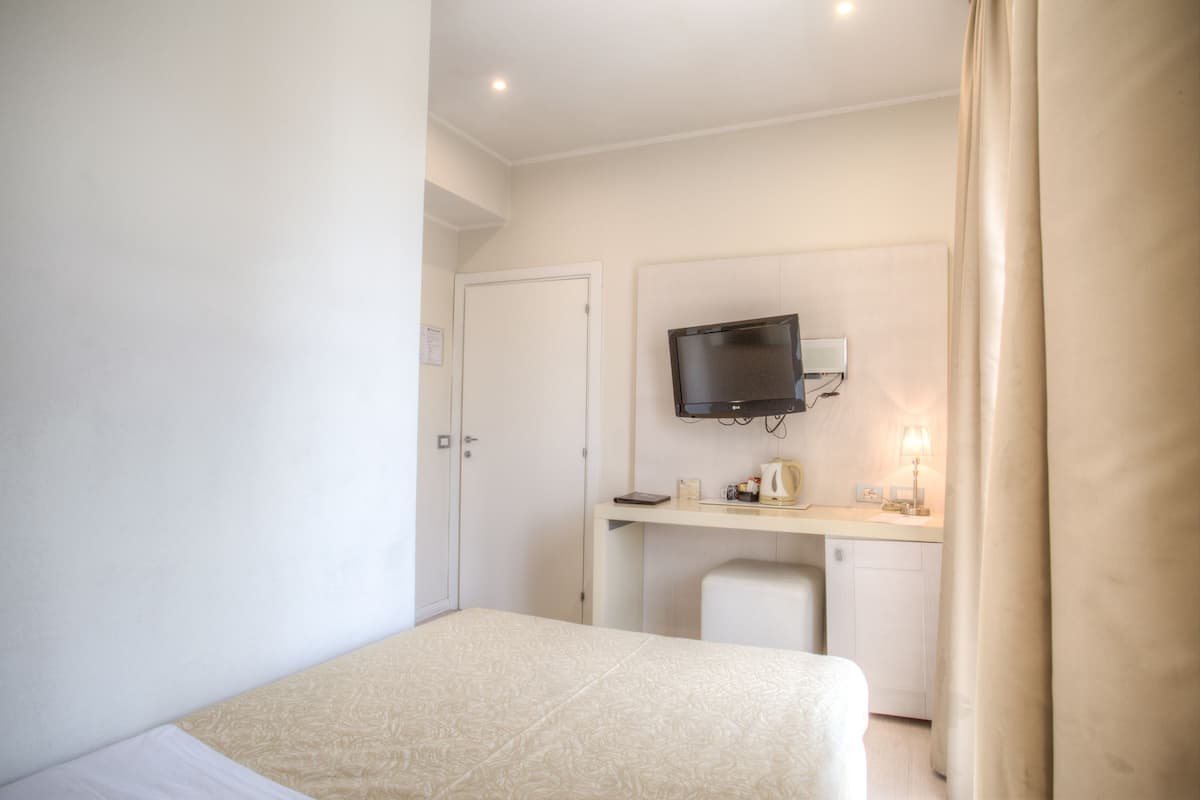 Una habitación de hotel con cama, escritorio con televisor y una silla pequeña.