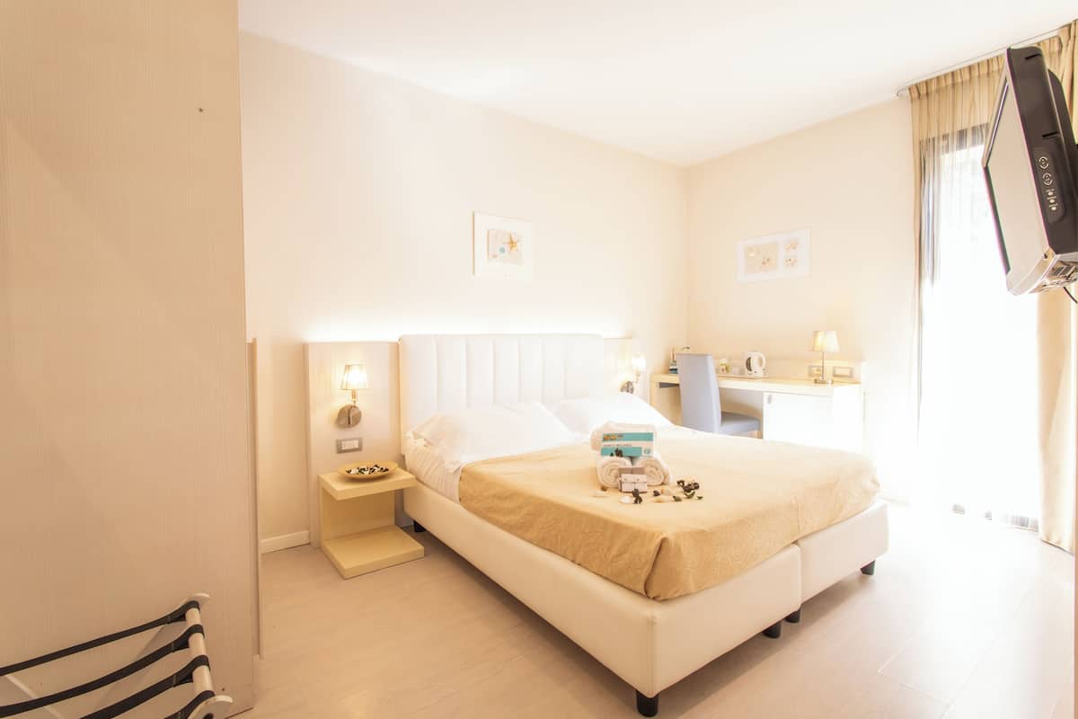 Habitación de hotel con cama, mesita de noche, lámpara y escritorio con silla.