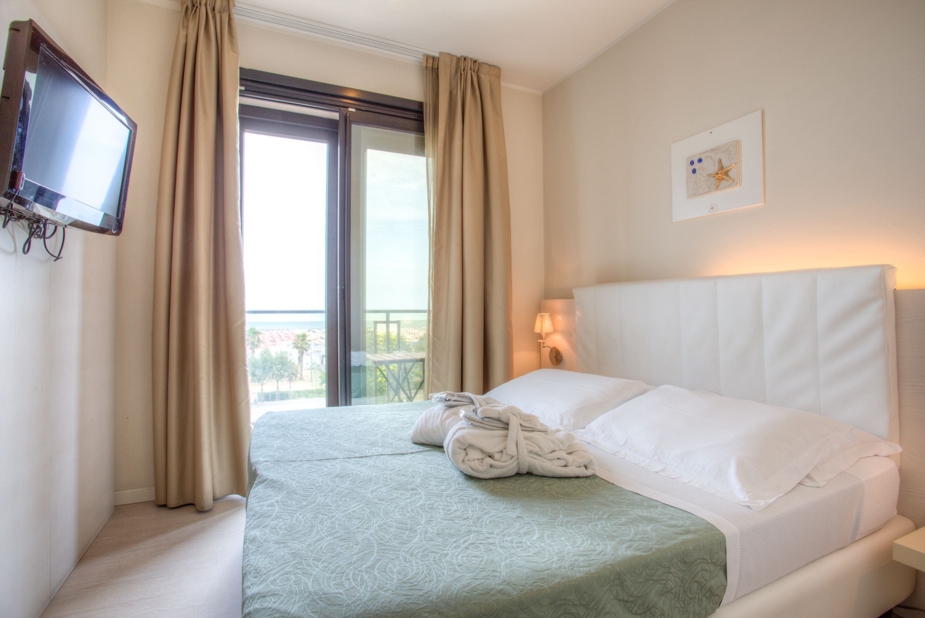 A hotel room with two beds, a TV, a balcony, and a painting on the wall.