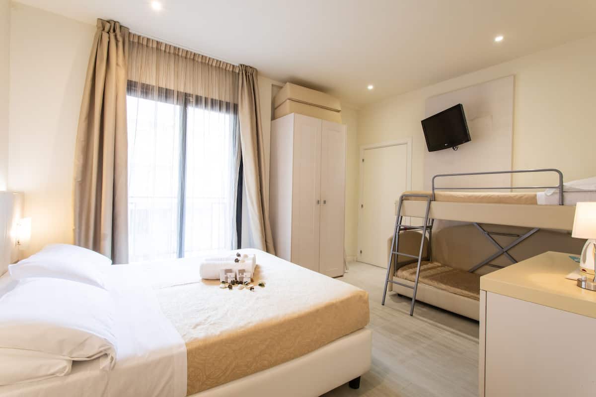 Una habitación de hotel con cama, escritorio, televisor y literas.
