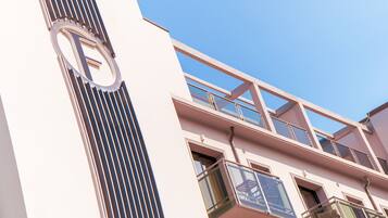 A building with a prominent 'F' logo, multiple balconies with glass railings, and a clear blue sky in the background.