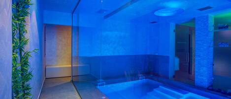 Un área de spa moderna con un jacuzzi de vidrio, una planta de bambú y una pared de piedra.