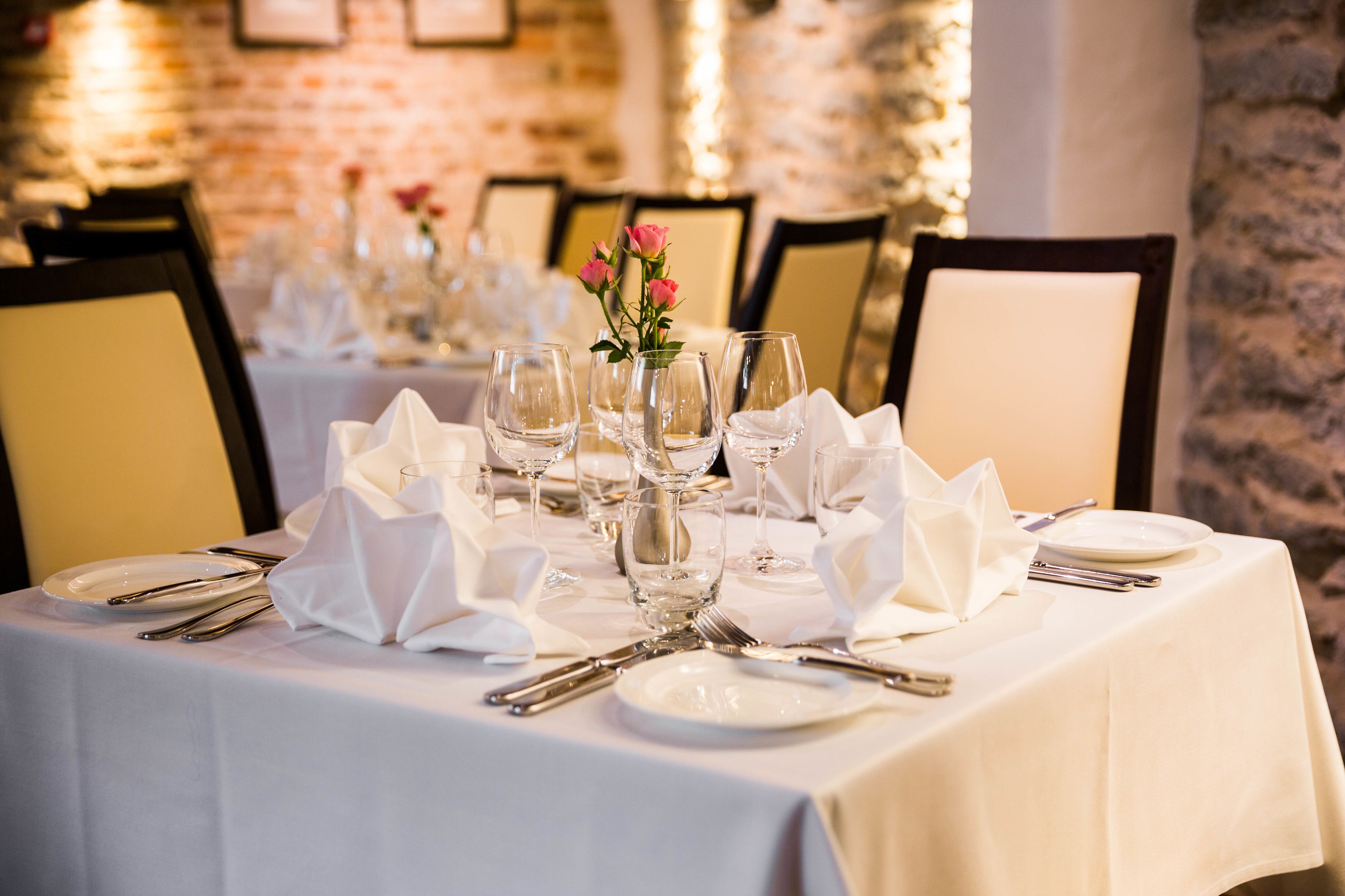 Une table à manger dressée avec une nappe blanche, des assiettes, des couverts et un vase rempli de fleurs roses.