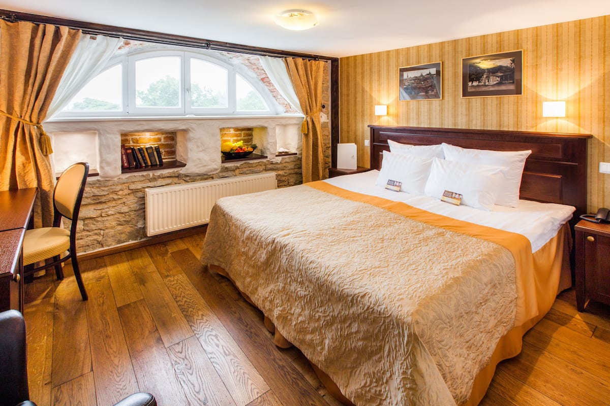 Une chambre d’hôtel avec un grand lit, une cheminée en pierre, une fenêtre avec des rideaux et un plancher en bois.
