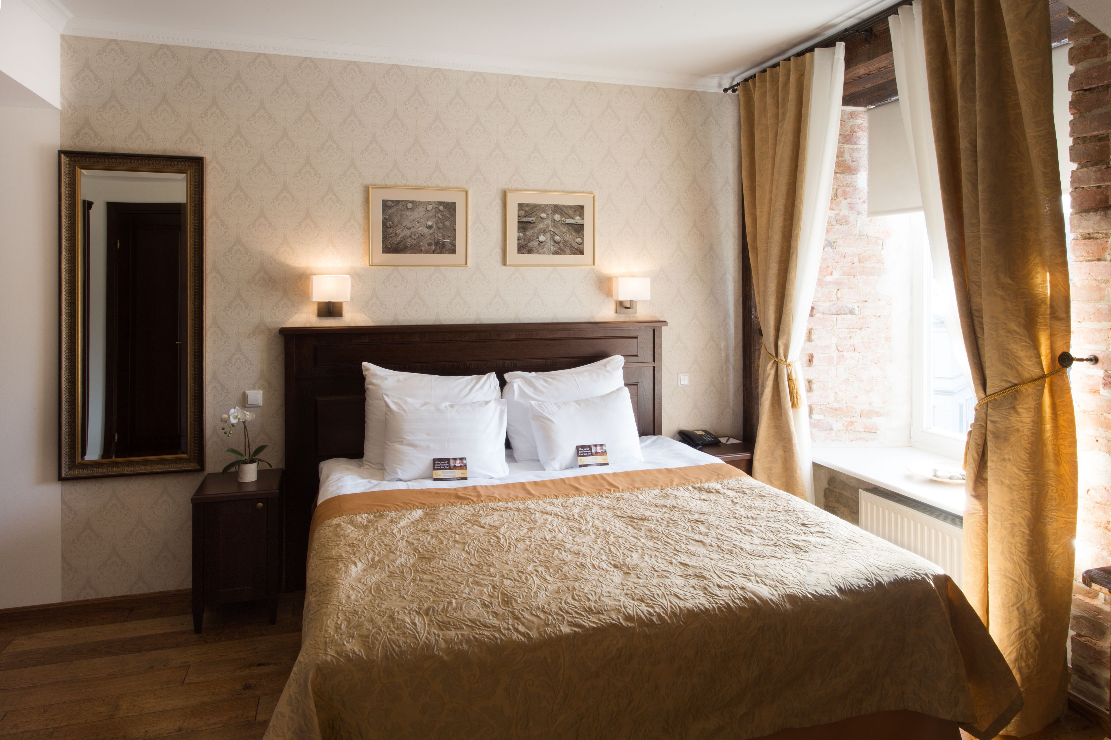 Een netjes opgemaakt bed met een hoofdbord, een nachtkastje met een lamp, en twee ingelijste foto's aan de muur.