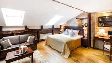 Ein Schlafzimmer mit einem großen Bett, einer Couch, einem Schreibtisch und einem Heizkörper. Es gibt Dachfenster und eine Backsteinwand.