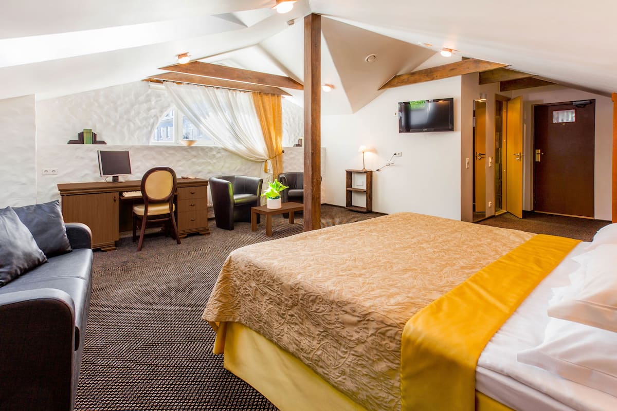 Une chambre d’hôtel avec un lit, un bureau avec un ordinateur, une chaise, une petite table avec une plante et un téléviseur fixé au mur.