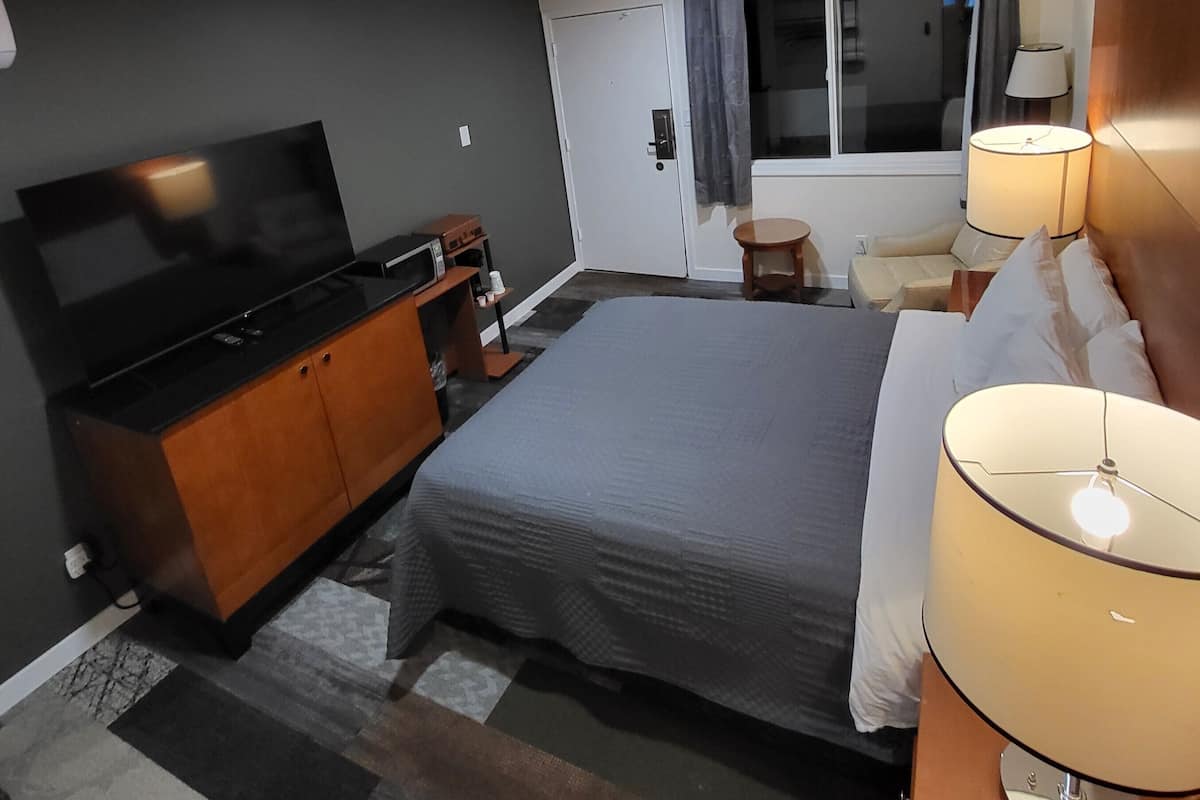 A hotel room with a bed, a TV, a desk, a lamp, and a window with curtains.