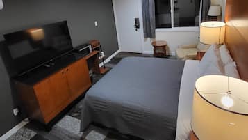 A hotel room with a bed, a TV, a desk, a lamp, and a window with curtains.