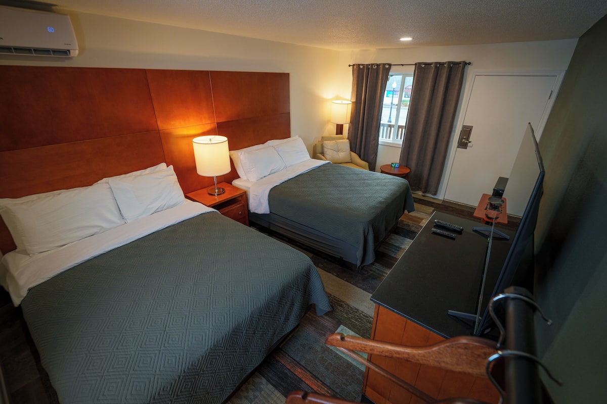 A hotel room with two beds, a desk, a chair, a TV, and a window with curtains.