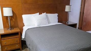 Uma cama bem arrumada com um edredom cinzento, duas mesas de cabeceira com abajures e uma cabeceira de madeira.