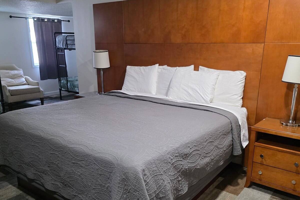 A hotel room with a large bed, a wooden headboard, two bedside tables with lamps, a chair, and a wardrobe.