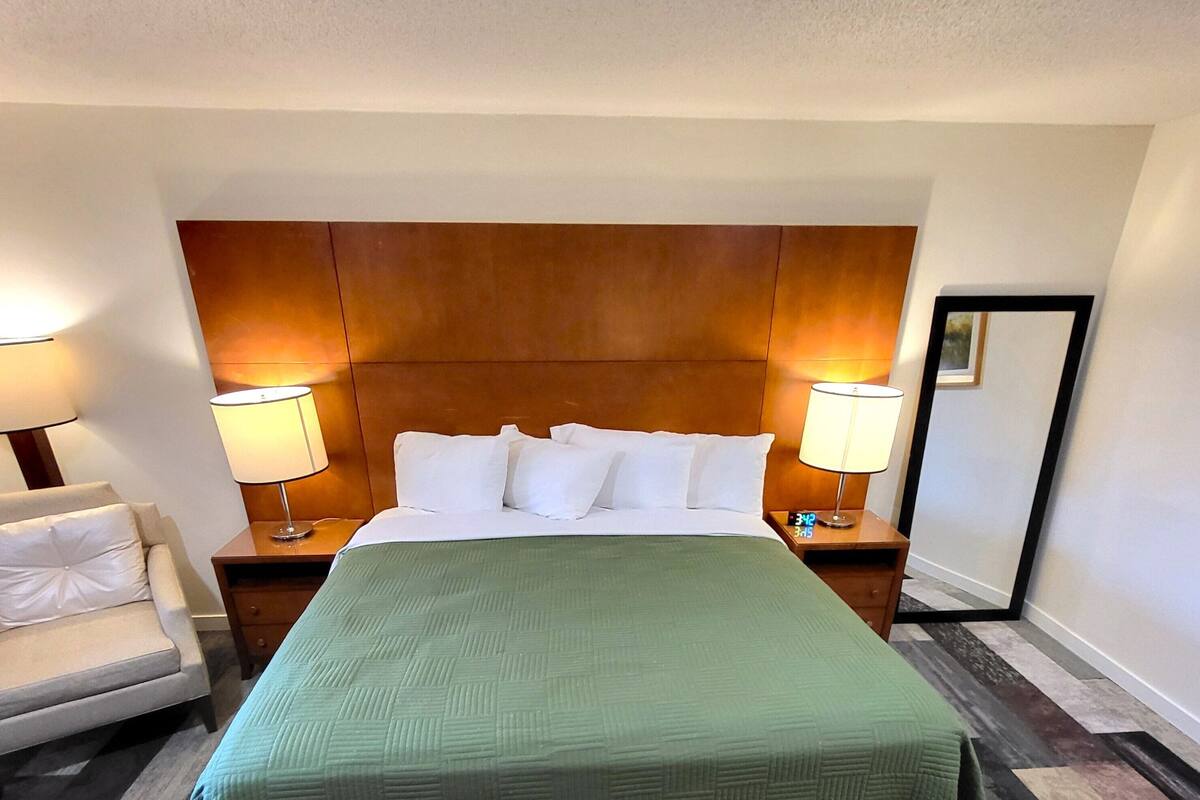 A hotel room with a large bed, two bedside lamps, a nightstand, a chair, and a mirror.