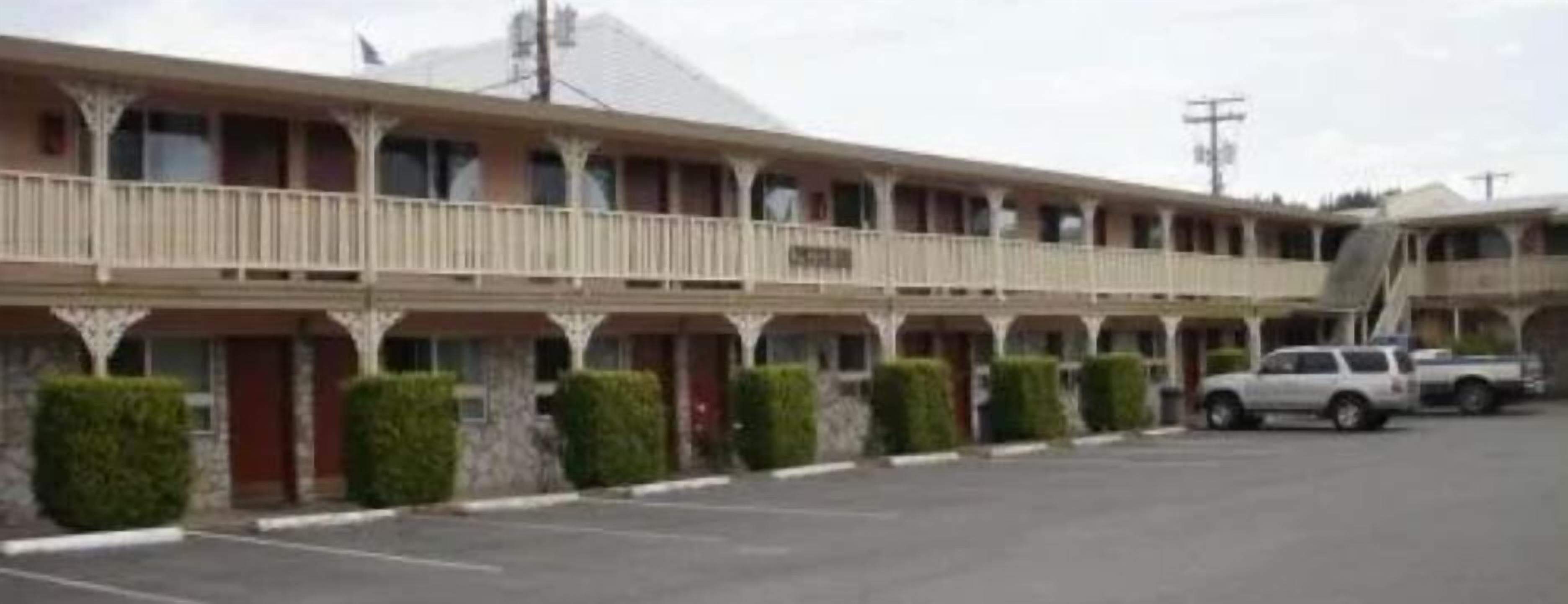 Motel amb una fila de habitacions, una zona de pàrquing coberta i un camió aparcat a l'exterior.