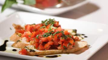 A square plate with a dish of bruschetta topped with diced tomatoes, herbs, and a drizzle of olive oil.