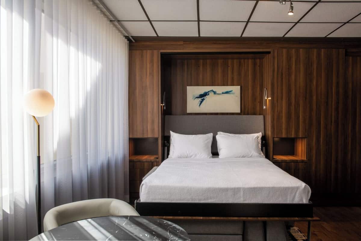 Una habitación de hotel moderna con una cama grande, una mesita de noche, una silla y un cuadro en la pared.
