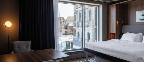 A hotel room with a large window, a bed, a desk, and a chair.