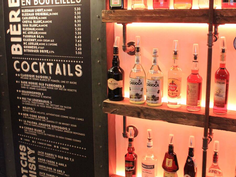 Una zona de bar con estantes llenos de botellas de licores y un menú que ofrece diversas bebidas.