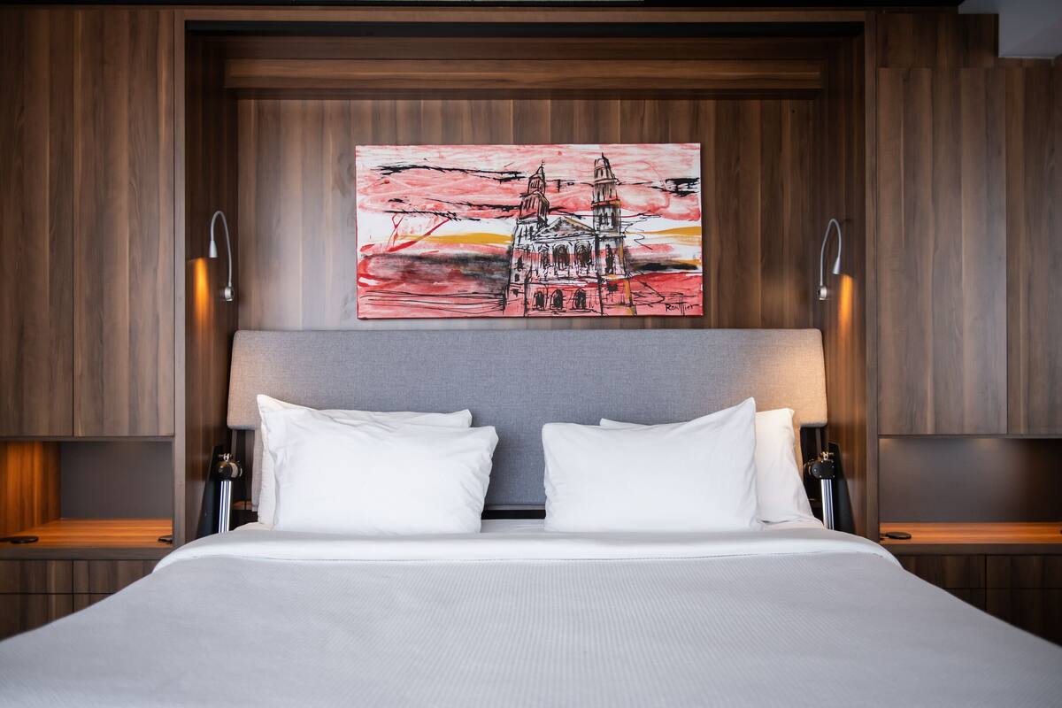 A hotel room with a large bed, two bedside tables, a wall-mounted painting, and a modern headboard.