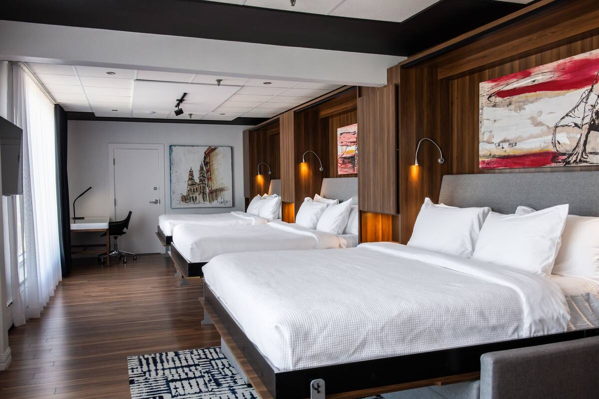 A modern hotel room with two beds, a desk, and a large abstract painting on the wall.