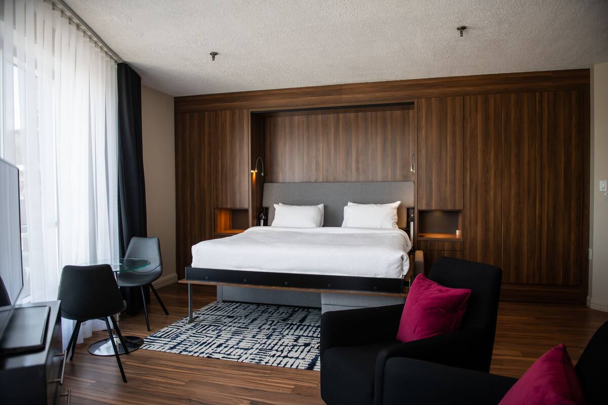 A modern hotel room with a large bed, a desk, and a chair.