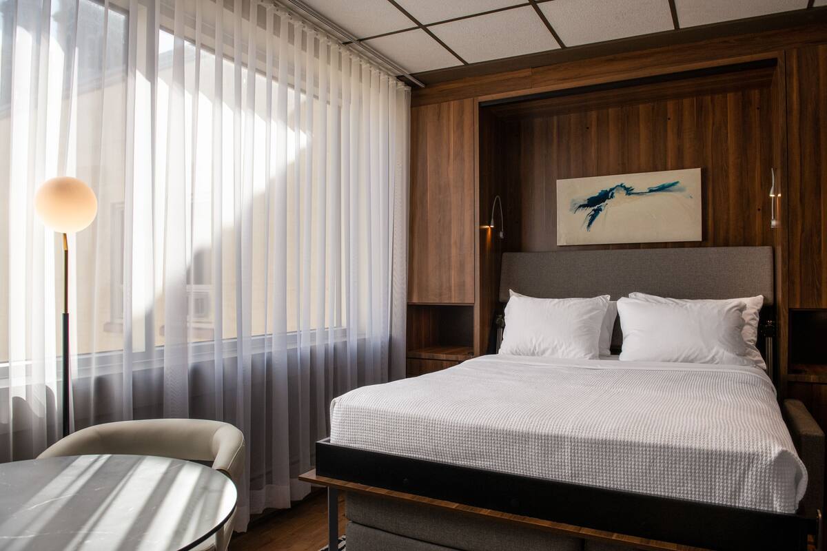 A hotel room with a bed, a table, and a chair.