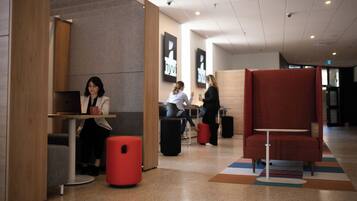 Un área de descanso moderna con diferentes disposiciones de asientos, incluyendo un banco rojo y una mesa con un ordenador portátil.