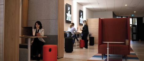 Un área de descanso moderna con diferentes disposiciones de asientos, incluyendo un banco rojo y una mesa con un ordenador portátil.