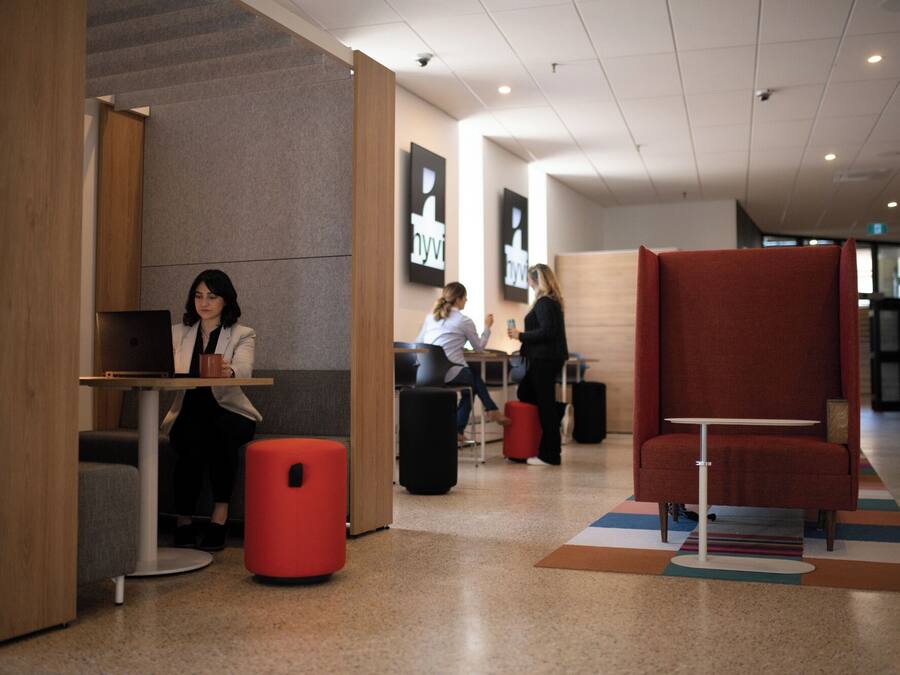 Un área de descanso moderna con diferentes disposiciones de asientos, incluyendo un banco rojo y una mesa con un ordenador portátil.