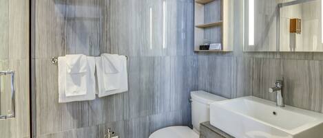 A modern bathroom with a marble backsplash, a white toilet, a sink with a mirror above it, and two towels hanging on a rack.