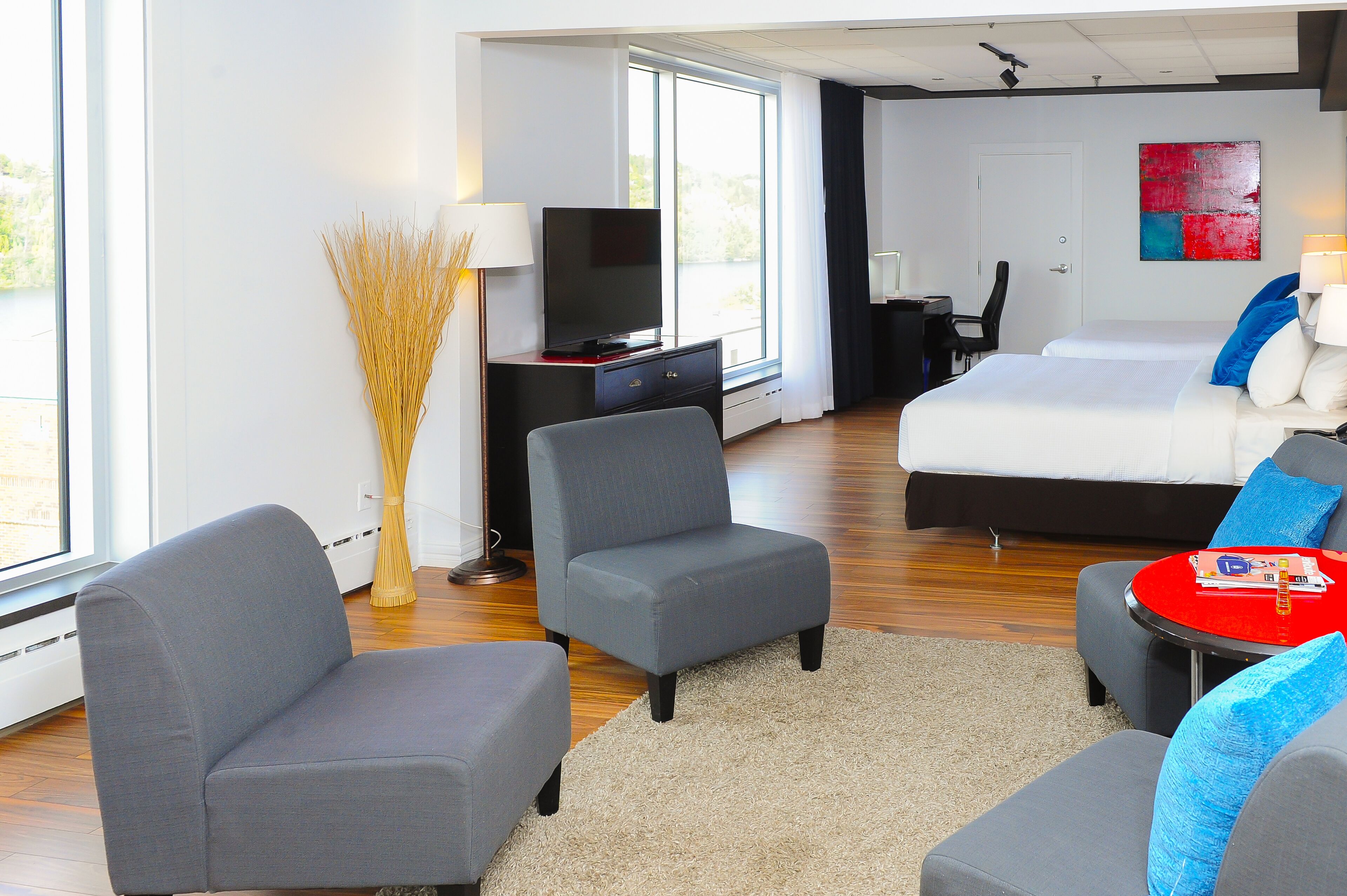 A modern hotel room with a large bed, two armchairs, a TV, and a desk.