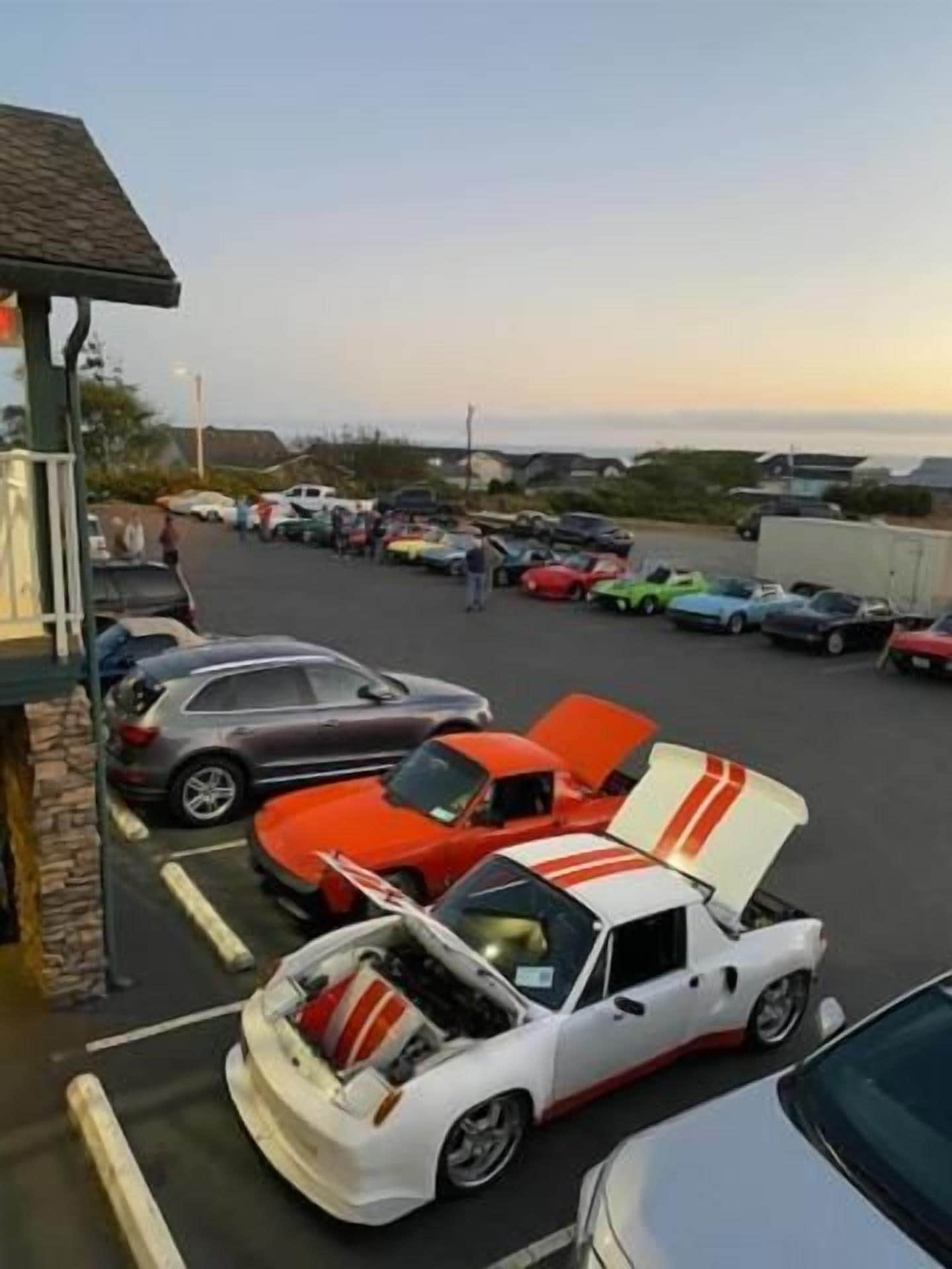 A parking lot with various cars, including a white car with its hood open.