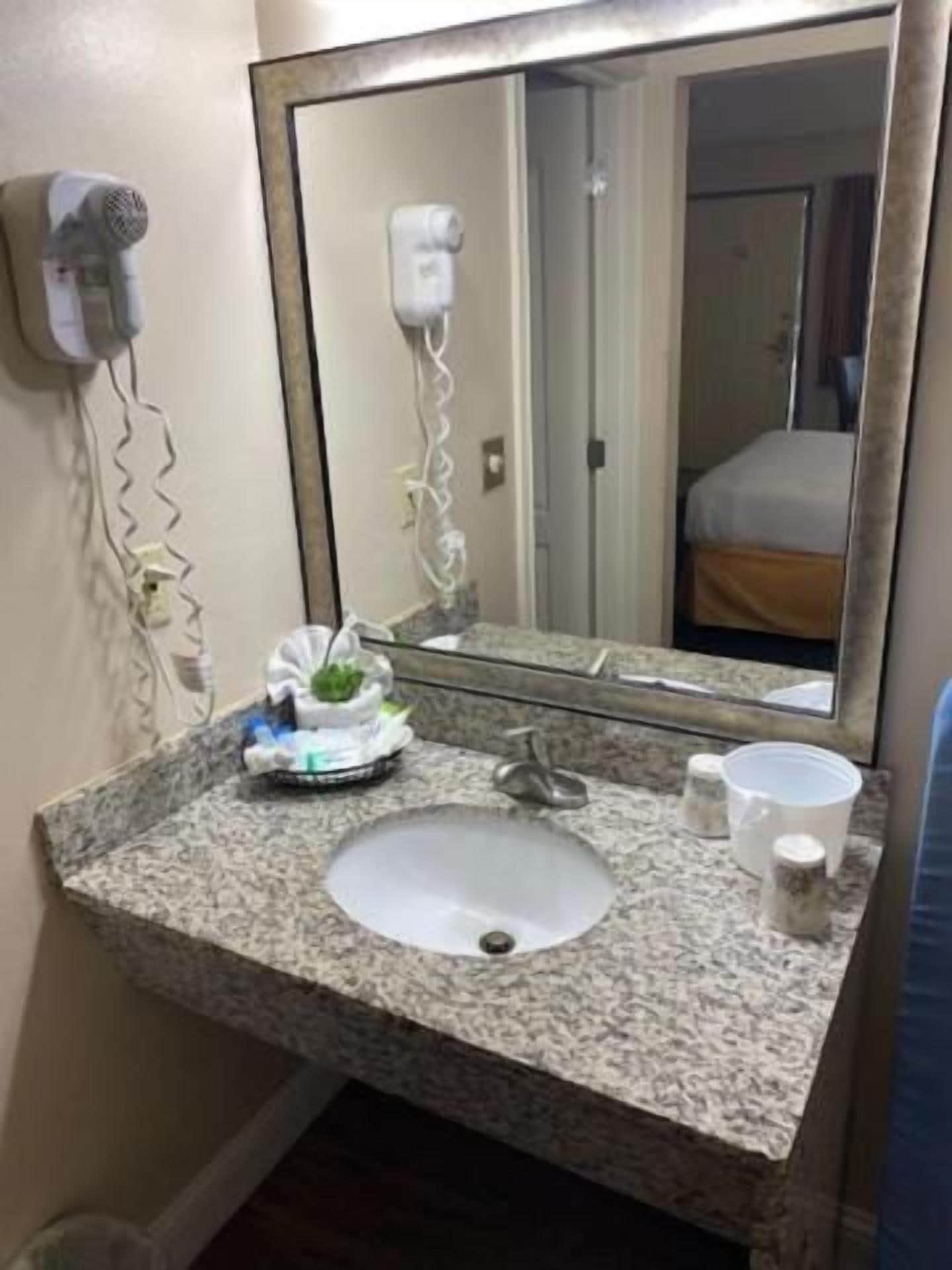 A bathroom with a granite sink, a mirror, a hairdryer, and a bottle.