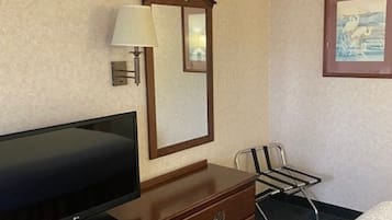 Habitación de hotel con una cama, un televisor sobre un aparador de madera, una silla, un espejo y un cuadro en la pared.