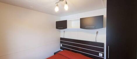 A bedroom with a bed, a wardrobe, and two wall-mounted speakers.