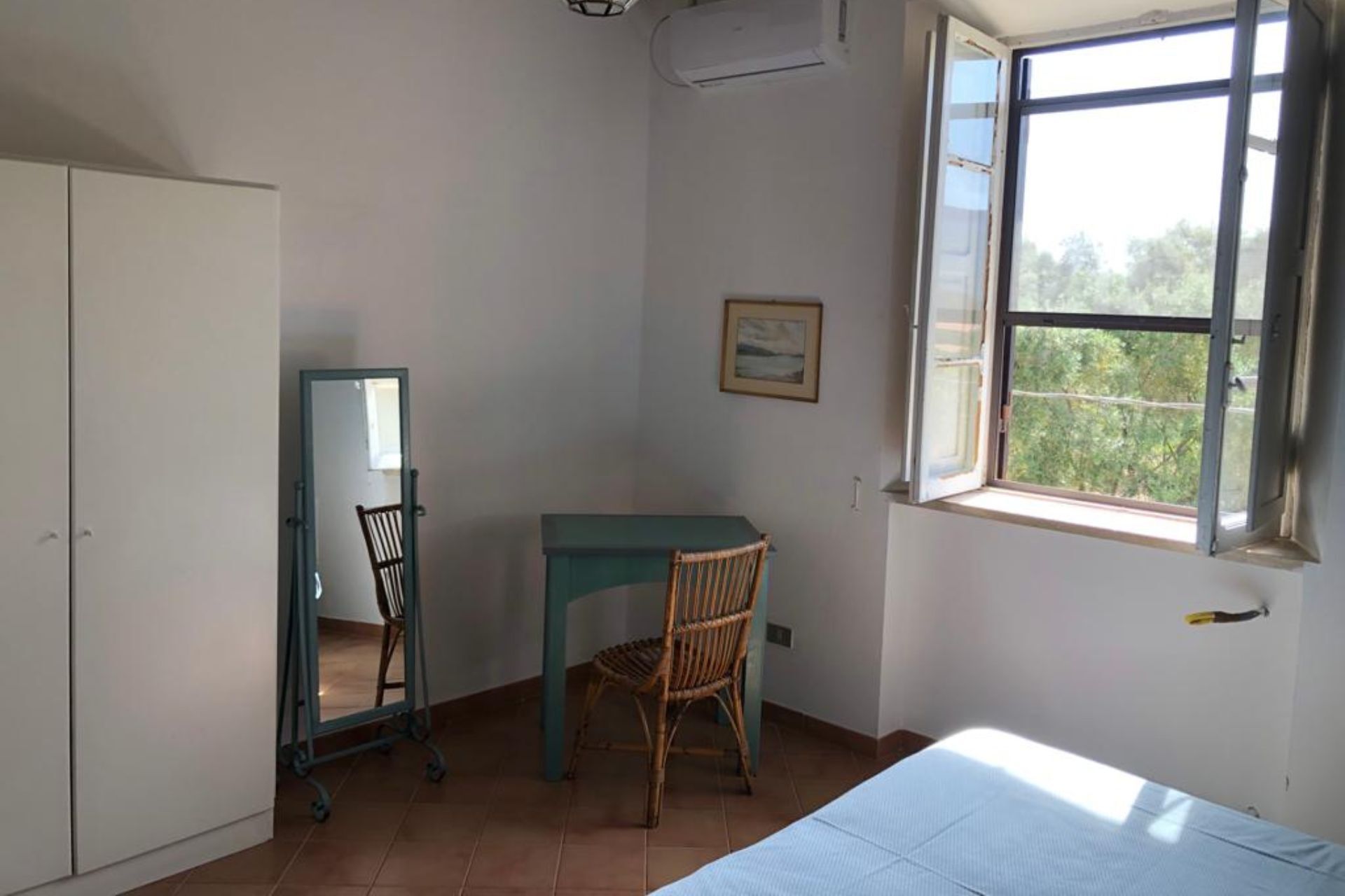 A room with a bed, a desk, a chair, a wardrobe, and a window with a view of trees.