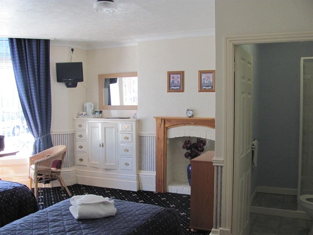 A hotel room with a bed, a dresser, a television, a mirror, and a fireplace.