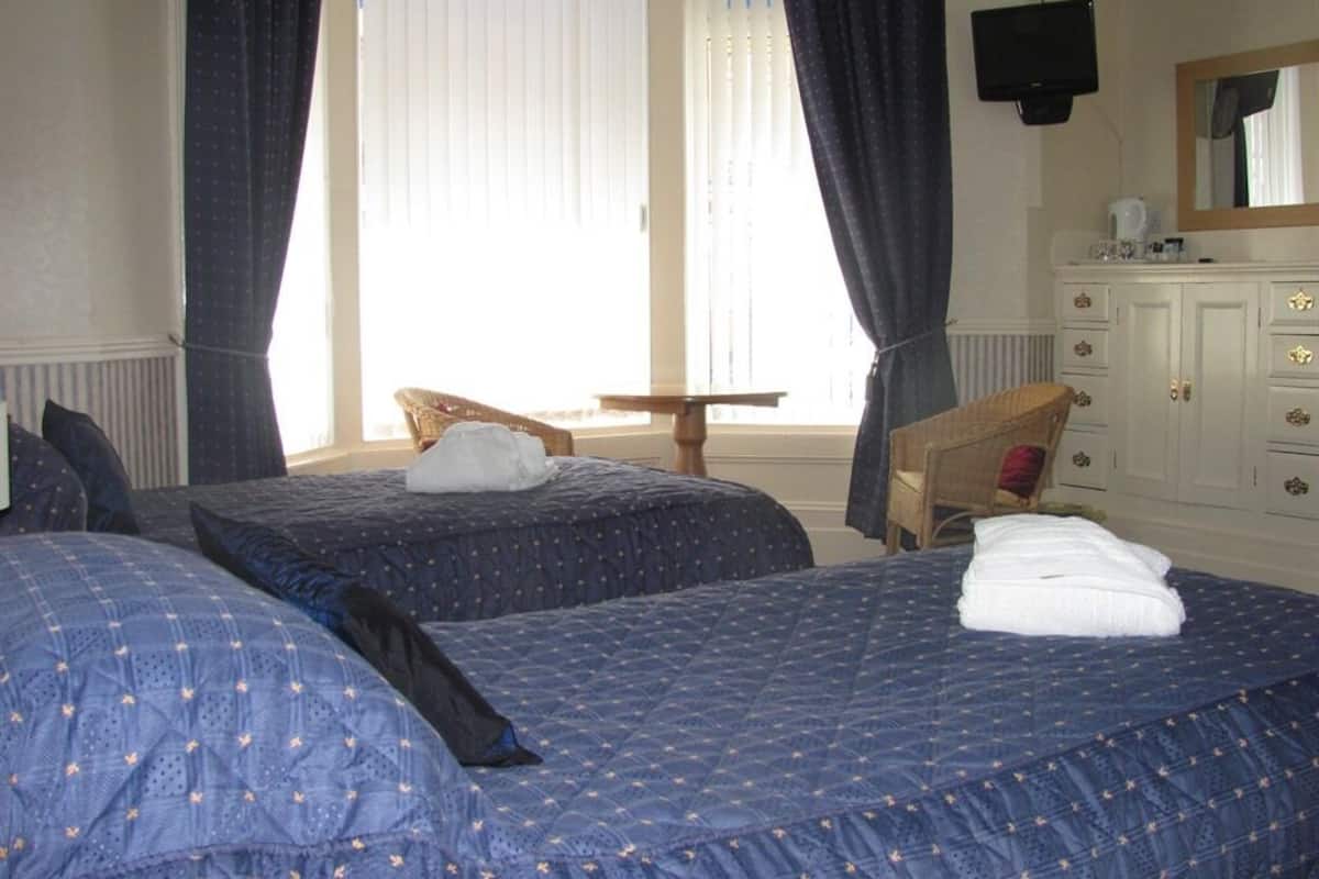 A hotel room with two beds, a small table, a chair, a dresser, and a TV mounted on the wall.