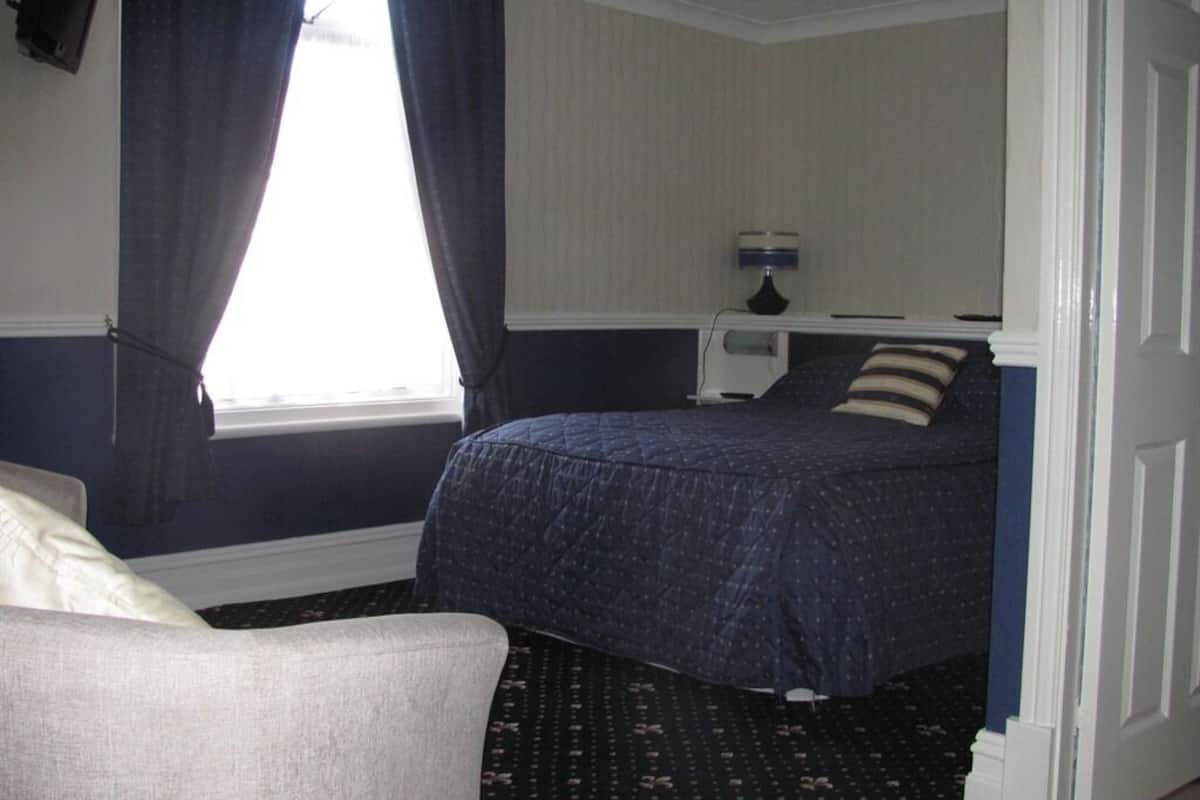 A bedroom with a bed, a nightstand, a lamp, and a window with curtains.
