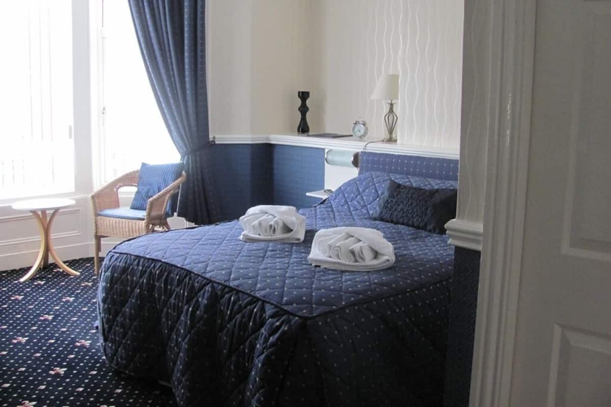 A hotel room with a bed, a chair, a lamp, and a window with curtains.