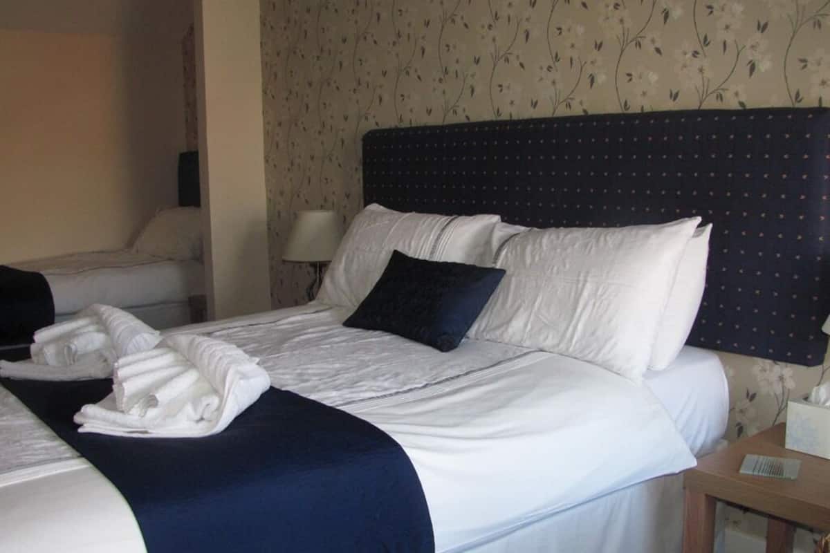 A hotel room with a neatly made bed, a bedside table with a lamp, and floral wallpaper.