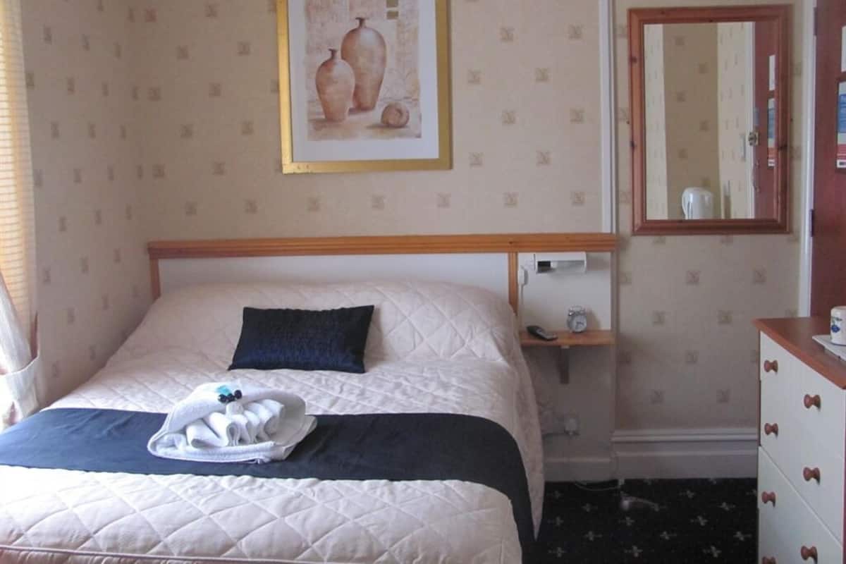A hotel room with a bed, a bedside table, a dresser, a mirror, and a framed picture on the wall.