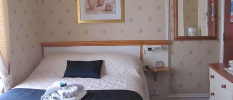 Una habitación de hotel con cama, mesita de noche, cómoda, espejo y un cuadro enmarcado en la pared.