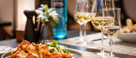 Une table à manger avec une assiette de nourriture, des verres de vin blanc et une bouteille d’eau.