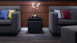 A modern living room with two grey sofas, each with colorful cushions, and a black ottoman with a potted orchid between them. - The Rilano Hotel Munich, Trademark Collection by Wyndham (Munich)