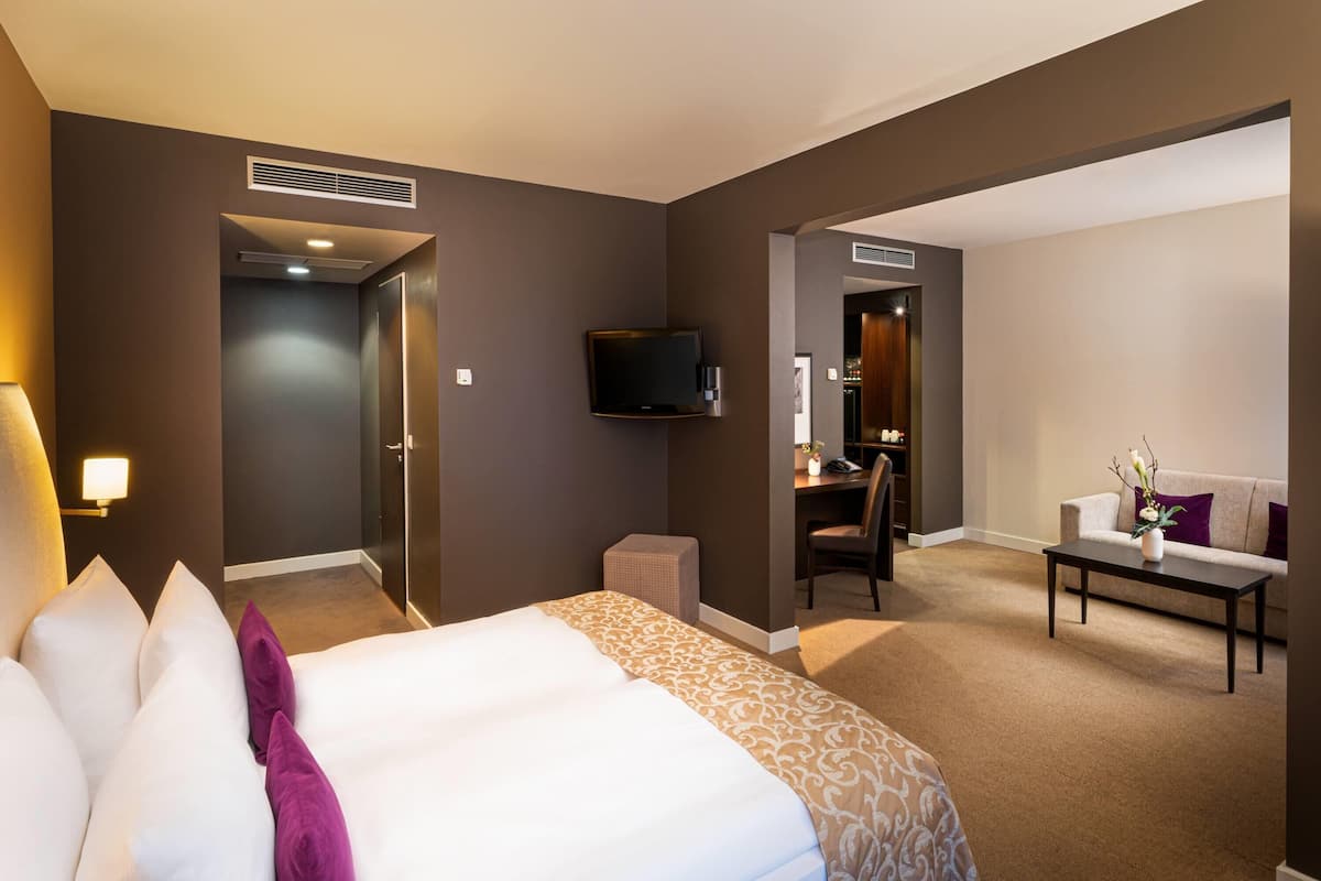 A hotel room with a bed, a desk, a television, and a seating area.