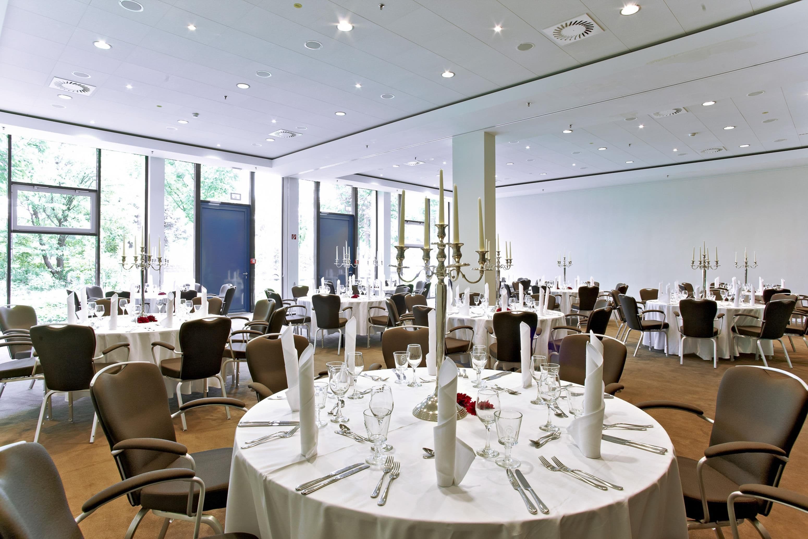 Een balzaal met ronde tafels gedekt voor een diner, met witte tafelkleden, bestek en kaarsen als middelpunt.