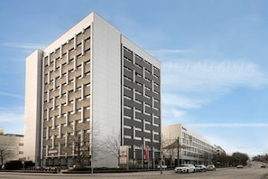 A multi-story building with a modern architectural design, featuring a prominent entrance and a parking area.